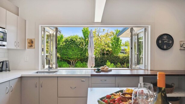 A modern kitchen with a large window, a clock, and a wine bottle on the counter.