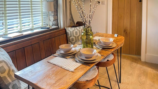 A wooden dining table with a placemat, set with bowls and plates, in a room with wooden flooring and a bench. - 2 bedroom accommodation in Kielder (Kielder)