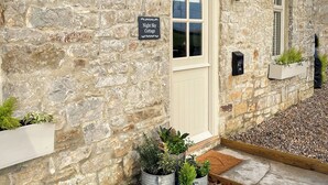 A stone cottage with a sign reading "Night Sky Cottage," a door, windows, and planters with greenery. - 2 bedroom accommodation in Kielder (Kielder)