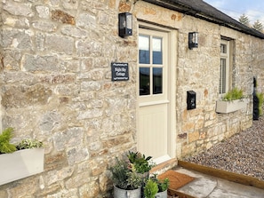 A stone cottage with a sign reading "Night Sky Cottage," a door, windows, and planters with greenery. - 2 bedroom accommodation in Kielder (Kielder)