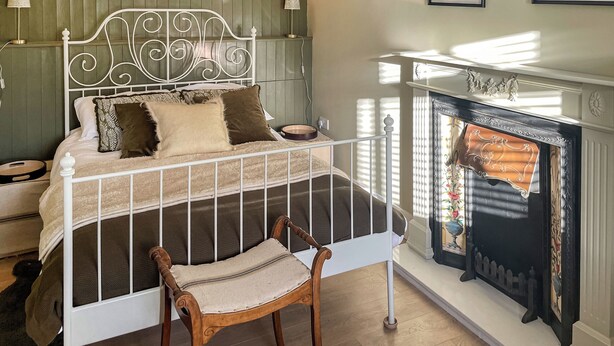 A bedroom with a white metal bed frame, a wooden chair, a fireplace, and framed botanical prints on the wall. - 2 bedroom accommodation in Kielder (Kielder)