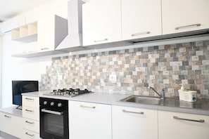 A modern kitchen with white cabinets, a tiled backsplash, a gas stove, and a sink.