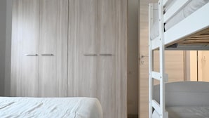 Une chambre avec un lit superposé, une armoire et une porte donnant sur une autre pièce.