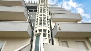 Un immeuble résidentiel à plusieurs étages, doté d’une tour centrale, de balcons et surplombant un ciel dégagé.