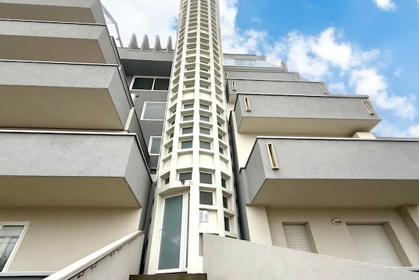A multi-story residential building with a central tower, balconies, and a clear sky.