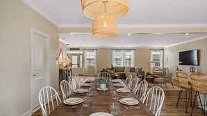 A dining room with a long wooden table set for six, white chairs, and a large woven light fixture above.