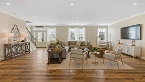 A spacious living room with a large sofa, two armchairs, a coffee table, and a TV mounted on the wall.