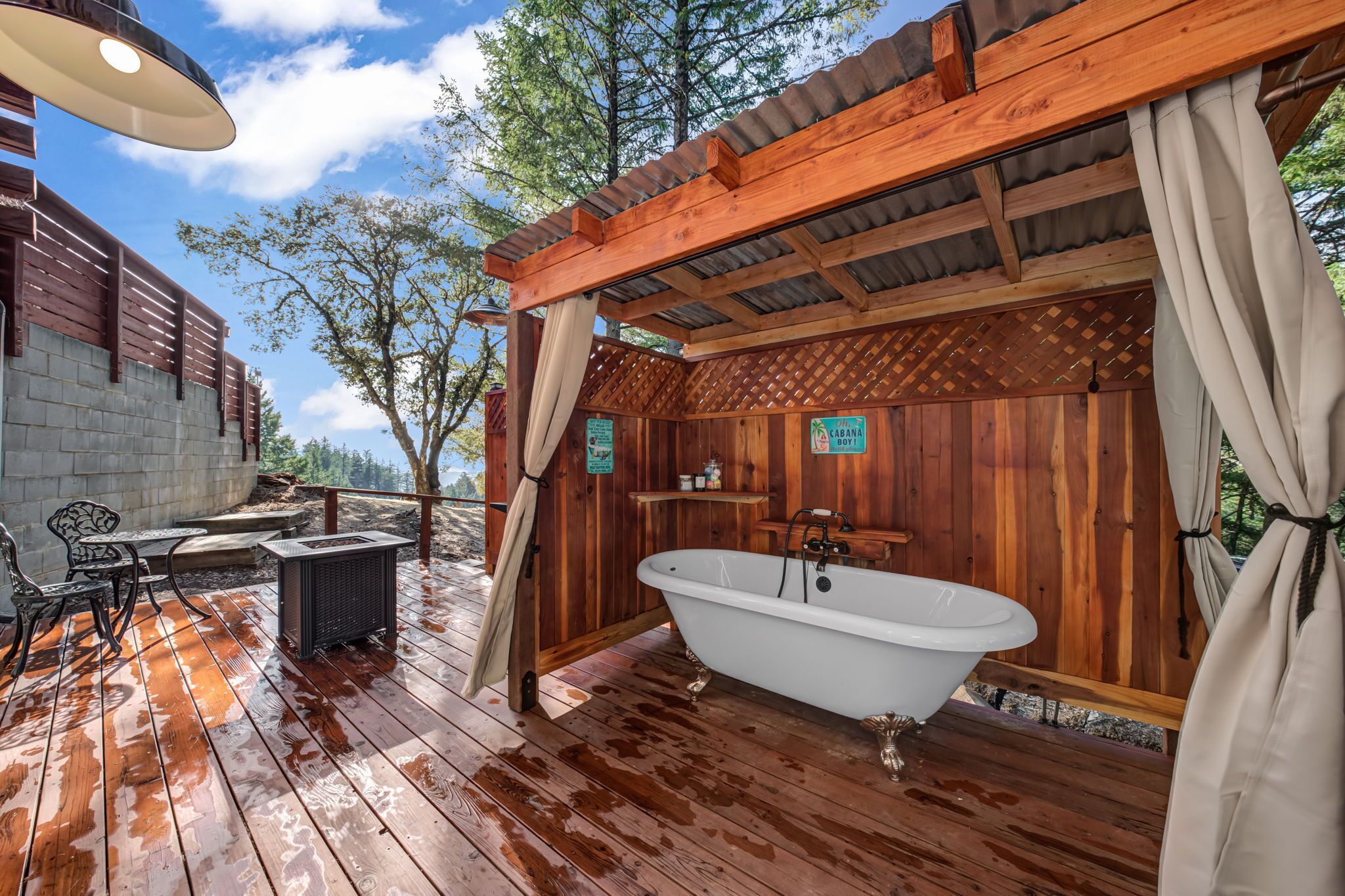 Eine Holzterrasse mit einer weißen Badewanne, Gartenmöbeln und einer Pergola.