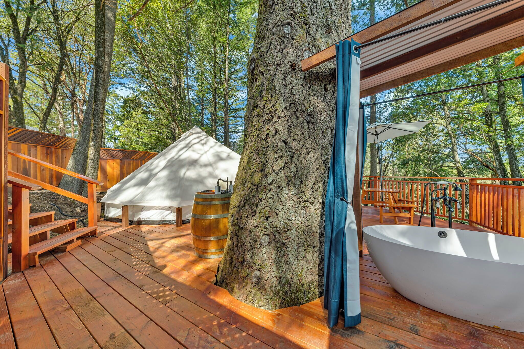 A wooden deck with a hot tub, a wooden fence, and a large tree.