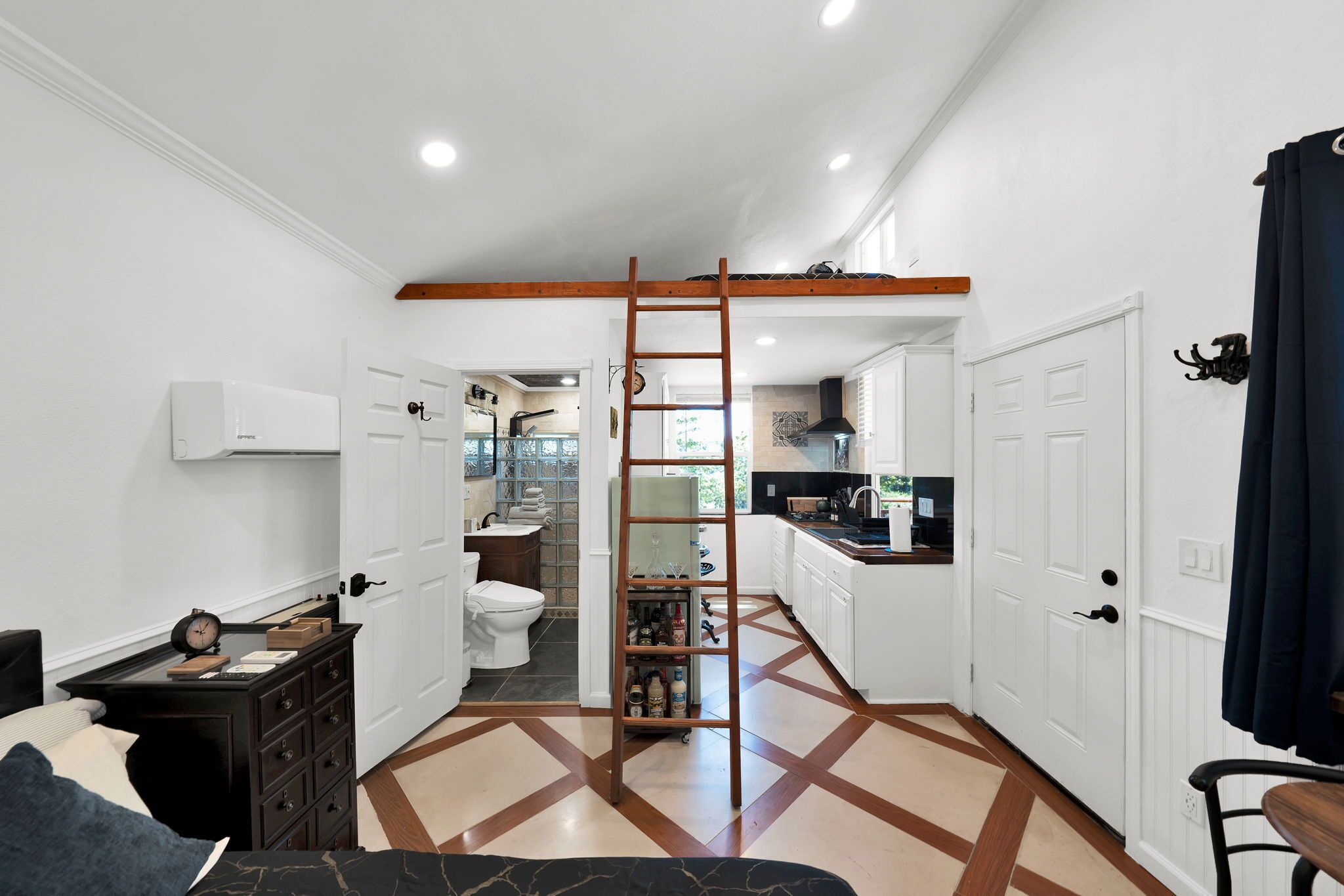 A compact kitchen with white cabinets, a wooden ladder, and a tiled floor.