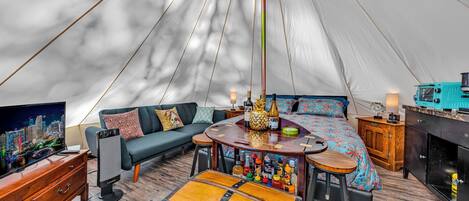 A tent interior with a sofa, a wooden table, a TV, and a storage trunk.