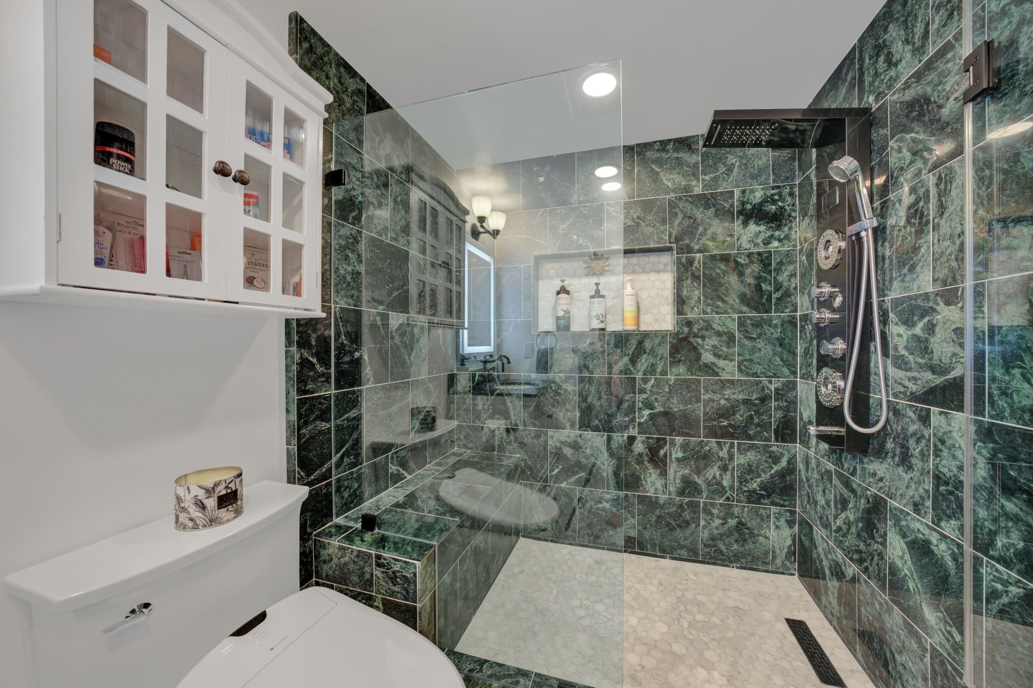 A modern bathroom with a glass shower enclosure, marble tiles, a toilet, and a cabinet with toiletries.