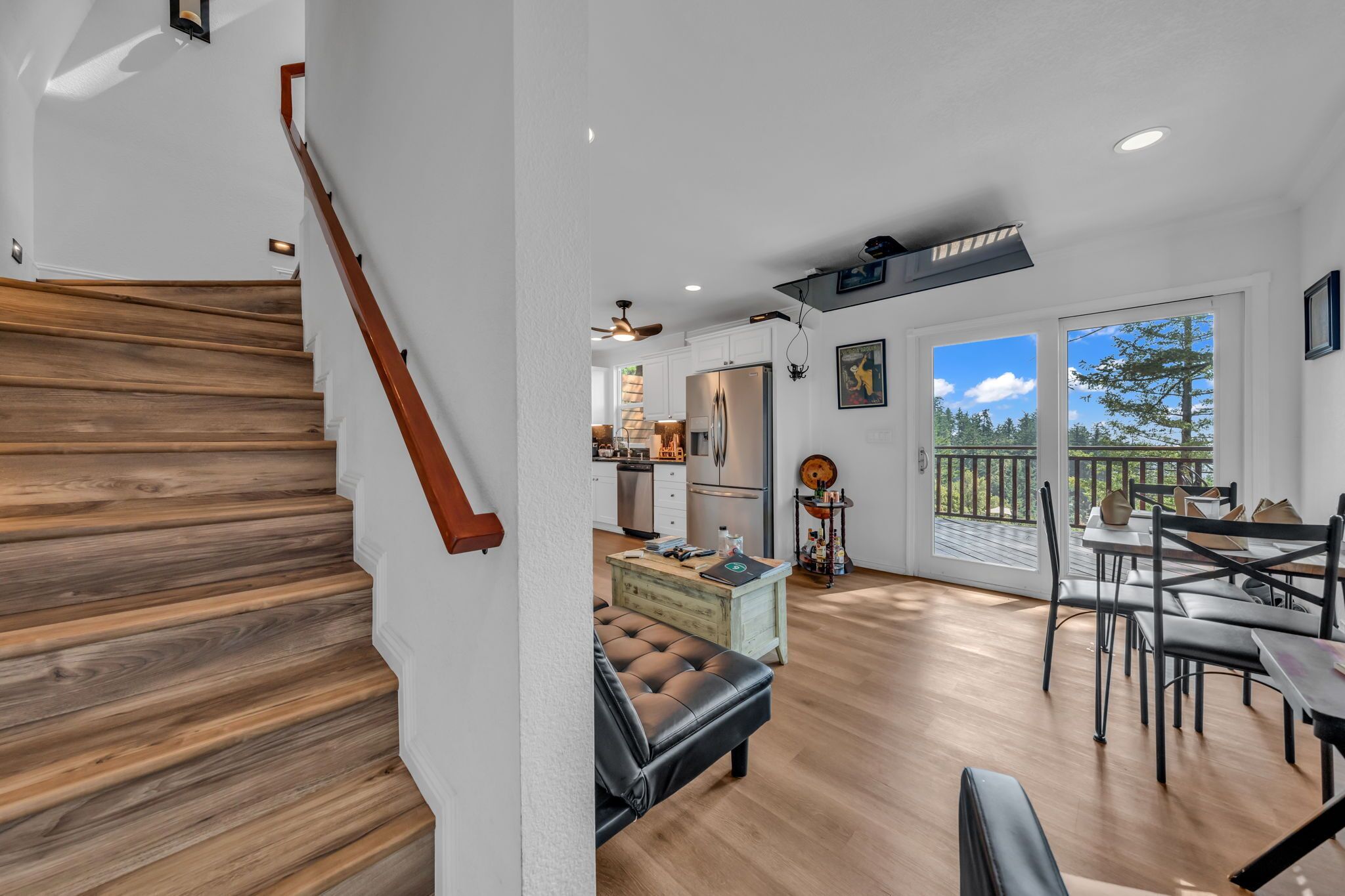 Amplia sala de estar con una escalera de madera, una mesa de comedor con sillas y vistas al exterior.