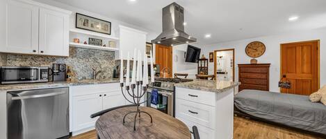 A compact kitchen with white cabinets, a built-in microwave, and a gas stove. There is a dining table with chairs and a decorative candelabra.