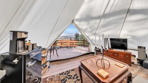 Een tent met een houten tafel, stoelen, een koffiezetapparaat en een televisie.