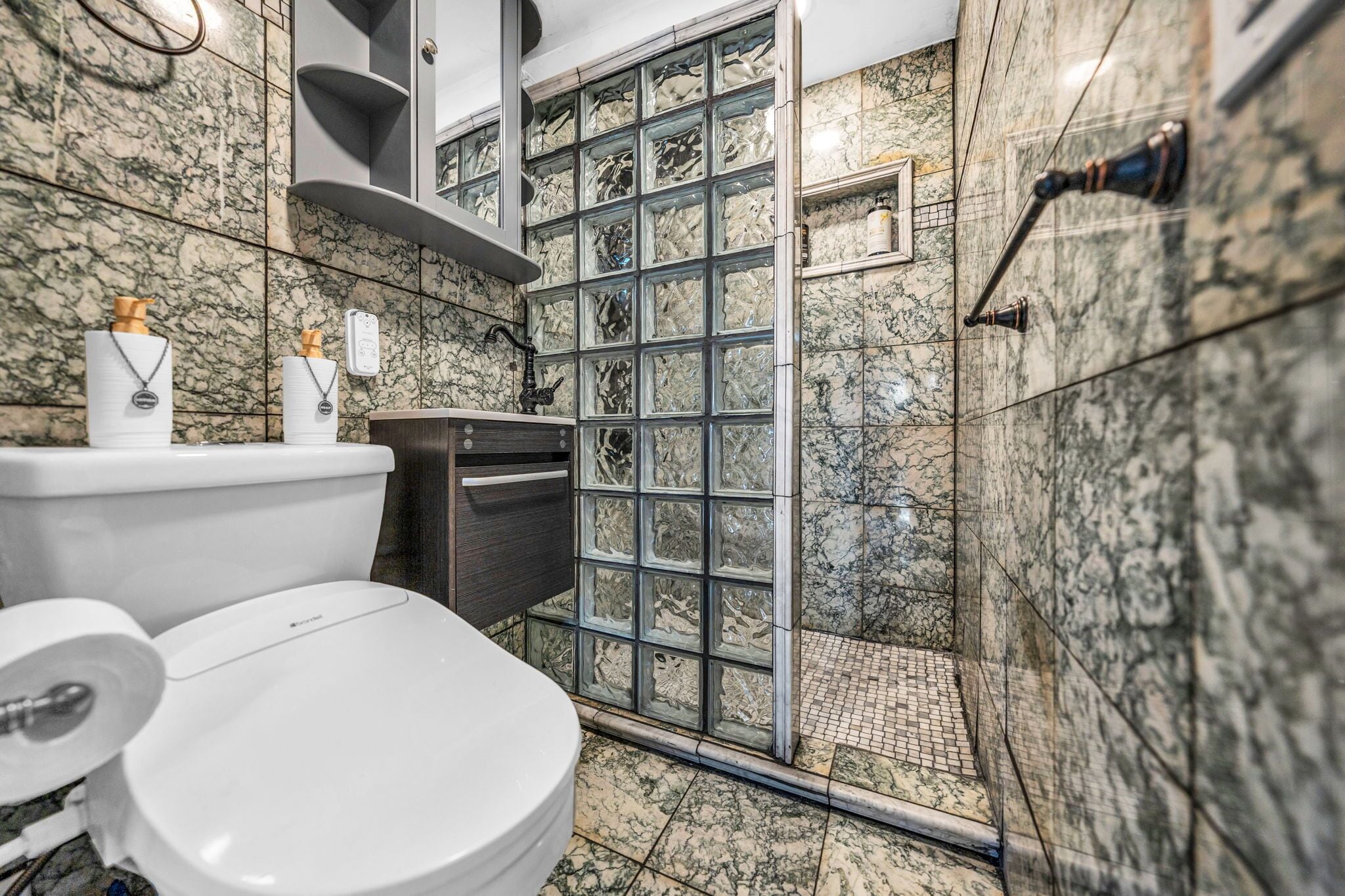 Un baño con pared de mármol, cabina de ducha de vidrio y un inodoro.