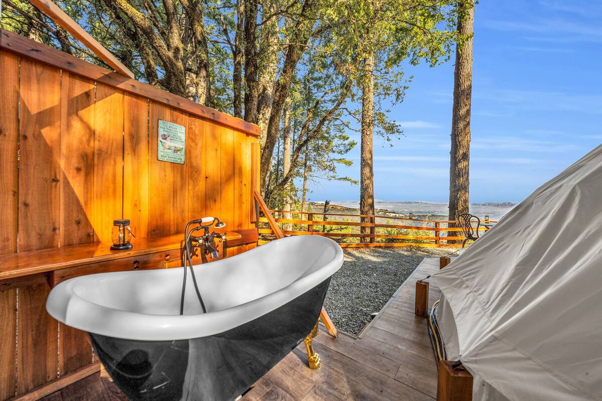 Une cabane en bois avec une baignoire, une terrasse en bois et une vue sur l’océan.