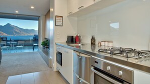 Une cuisine moderne équipée d’appareils électroménagers en acier inoxydable, une grande fenêtre donnant sur un paysage montagneux et un coin repas avec vue.