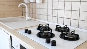 Een keuken met een witte kookplaat, vier kookzones, een witte gootsteen en een spatwand met vierkante tegels.