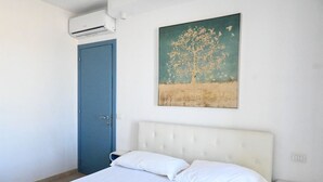 Een slaapkamer met een bed, een blauwe deur, een airconditioning en een schilderij van een boom.