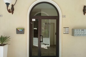 Entrada de hotel con puerta de vidrio, buzón y planta.