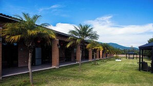A row of brick buildings with palm trees in front, a grassy area, and a gazebo in the distance. - Hotel Matea San Isidro  (Tonatico)