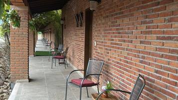 A covered outdoor seating area with brick walls and tiled flooring, featuring metal chairs with cushions.