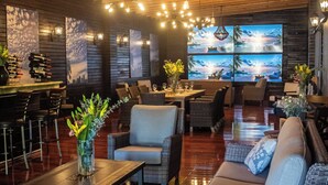A cozy lounge area with wicker furniture, a wooden ceiling, and a large TV screen displaying a beach scene. - Hotel Matea San Isidro  (Tonatico)