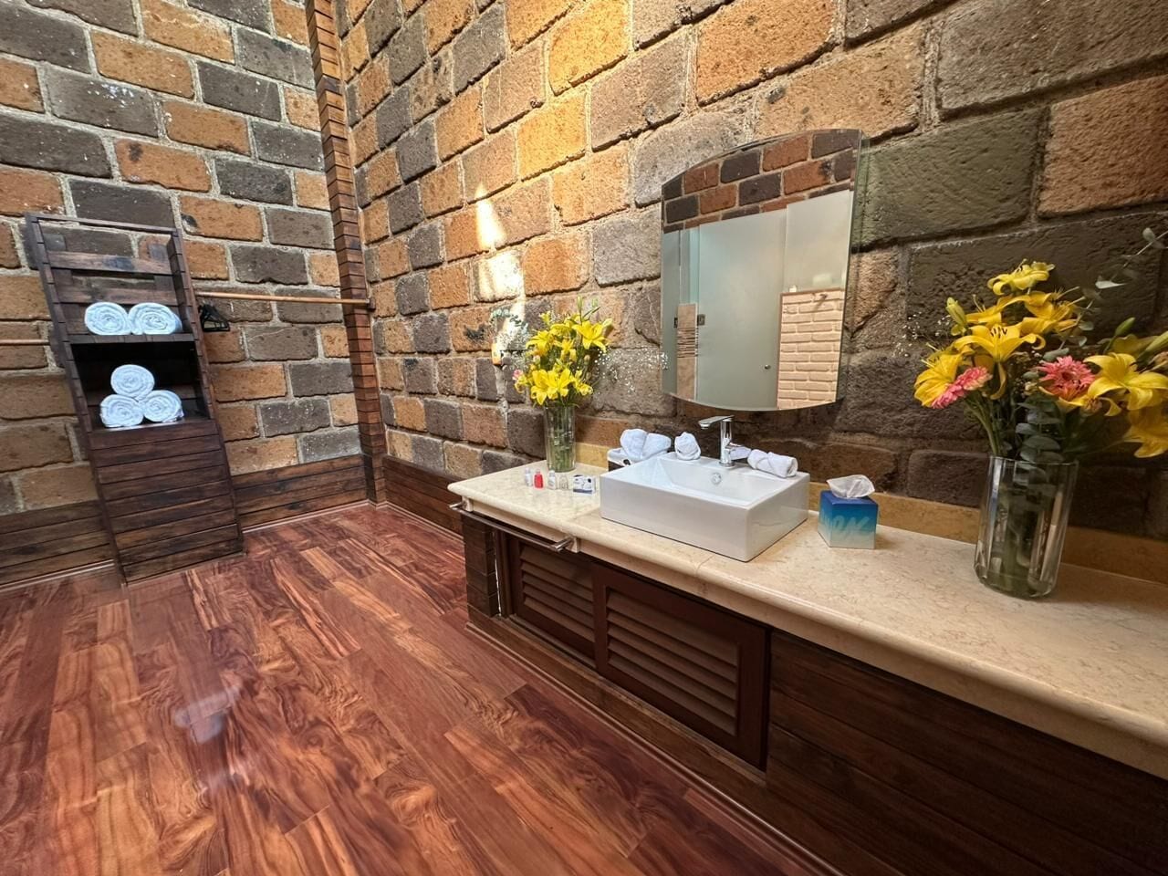 A bathroom with a wooden floor, a sink with a mirror, and two vases with flowers.