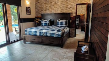 A bedroom with a large bed, a wooden headboard, a small bedside table, and a view of the outdoors through a sliding door.