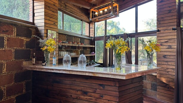 A rustic bar area with wooden beams, stone walls, and large windows offering views of greenery. - Hotel Matea San Isidro  (Tonatico)