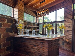 A rustic bar area with wooden beams, stone walls, and large windows offering views of greenery. - Hotel Matea San Isidro  (Tonatico)