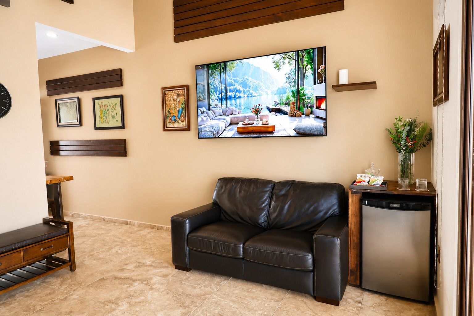 Una sala de estar con un sofá de cuero, un televisor de pantalla plana, una mesa de centro y una pequeña área de cocina con lavavajillas.