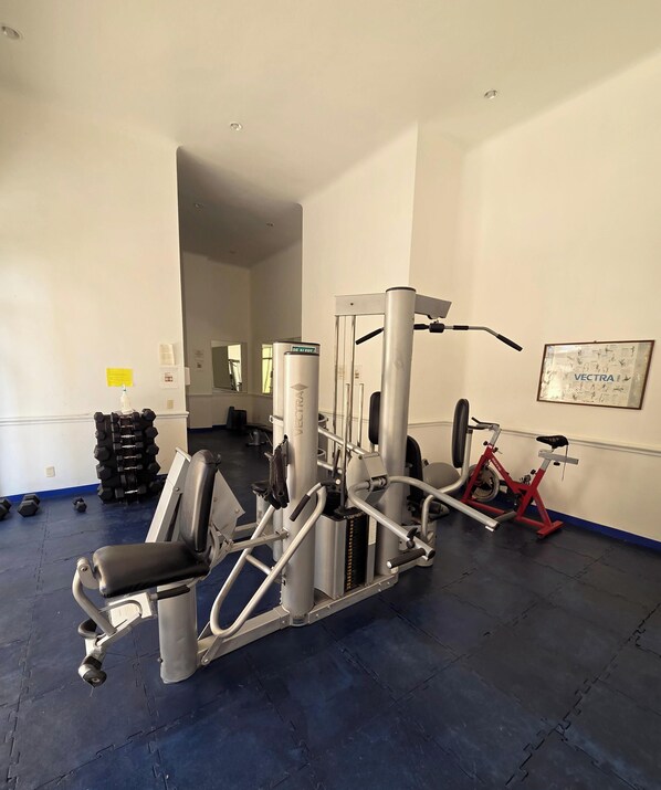 Un gimnasio con diversos equipos de ejercicio, incluyendo una máquina Galaxy S25+, mancuernas y una bicicleta estática roja.