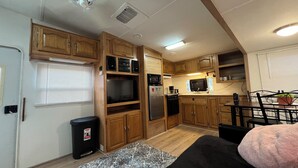 Cocina compacta para autocaravana con armarios de madera, microondas integrado y refrigerador.