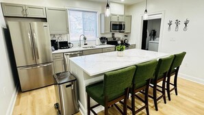 A modern kitchen with stainless steel appliances, a white marble island, and green upholstered chairs. - Feels Like Home - BBQ, Yard, Fire Pit (Fitchburg)