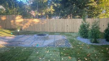 A backyard with a stone fire pit, a wooden fence, and a grassy area with scattered leaves.