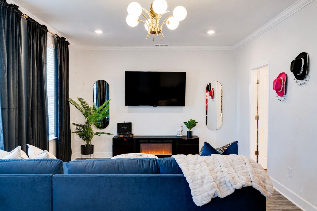 A modern living room with a large flat-screen TV, a fireplace, a sofa, and a ceiling light fixture.