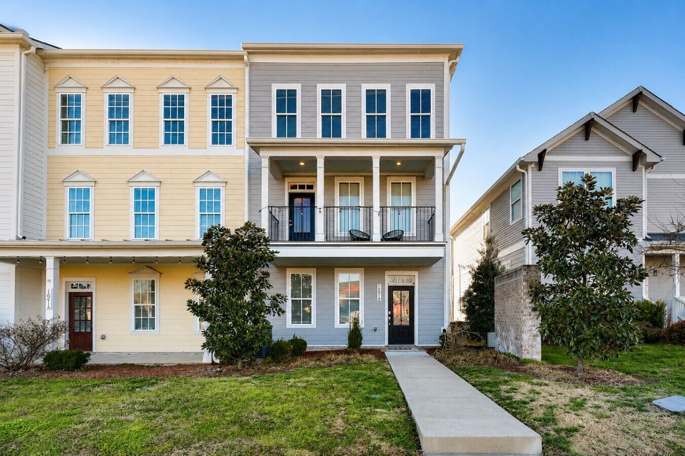 A multi-story residential building with a front porch, a balcony, and a driveway.