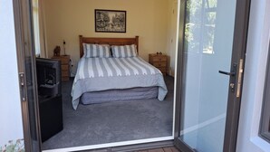 A bedroom with a bed, a nightstand, a lamp, a framed picture on the wall, and a sliding glass door.