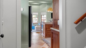A hallway leading to a dining area with a wooden table and chairs, a hanging pendant light, and a view of the outside through large windows. - Midnight Moon Retreat (Beaufort)