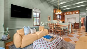 A spacious living room with a sofa, ottoman, and dining table. A flat-screen TV is mounted on the wall. - Midnight Moon Retreat (Beaufort)