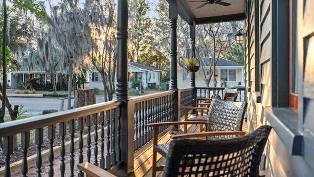 A covered porch with wooden chairs and a ceiling fan, overlooking a street with houses and trees. - Midnight Moon Retreat (Beaufort)