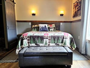 A bedroom with a bed, two wall-mounted lights, a bench, a door, and a window. - Bunker Hill Hideaway One-bedroom Suite (Austin)
