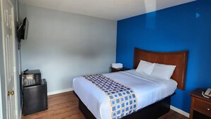 Ein Hotelzimmer mit Bett, Nachttisch, an der Wand montiertem Fernseher und Mülleimer.