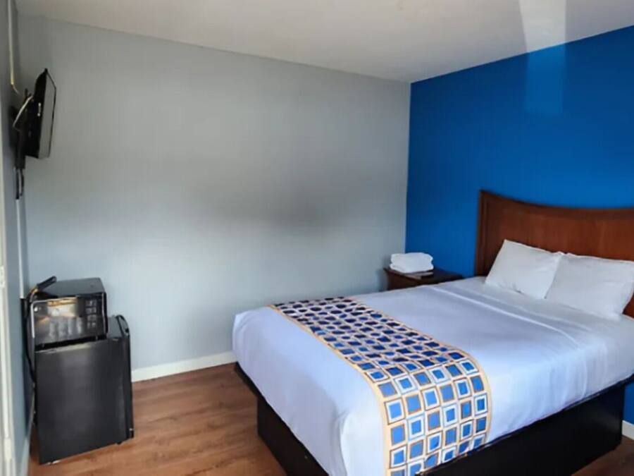 A hotel room with a bed, a nightstand, a TV mounted on the wall, and a trash bin.