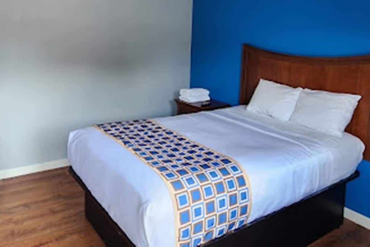 A neatly made bed with a patterned bedspread, a wooden headboard, and a nightstand with a phone.