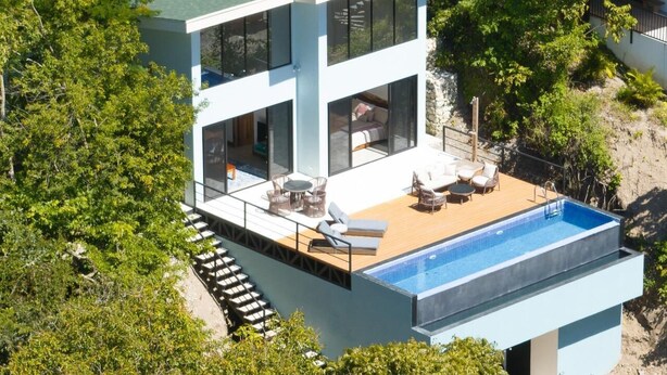 A modern two-story house with a rooftop air conditioning unit, a swimming pool, and outdoor furniture.