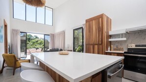 A modern kitchen with a large island, wooden cabinets, stainless steel appliances, and a view to the outdoors.