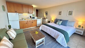 A compact hotel room with a kitchenette, a bed with a green blanket, a small table, and a green sofa. - Hilo Studio Retreat with Gorgeous Park View, AC, WiFi, Pool (Hilo)